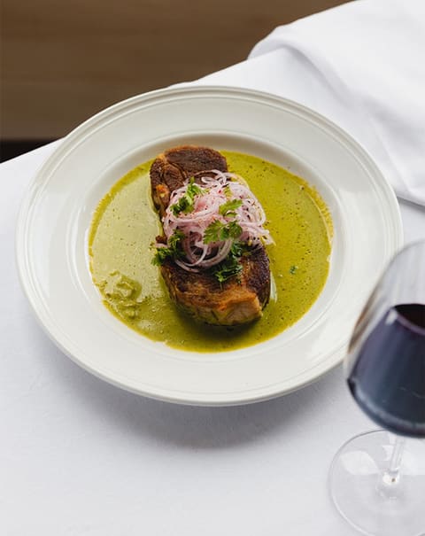Pièce rôtie, sauce verte aux herbes et oignons roses, verre de rouge